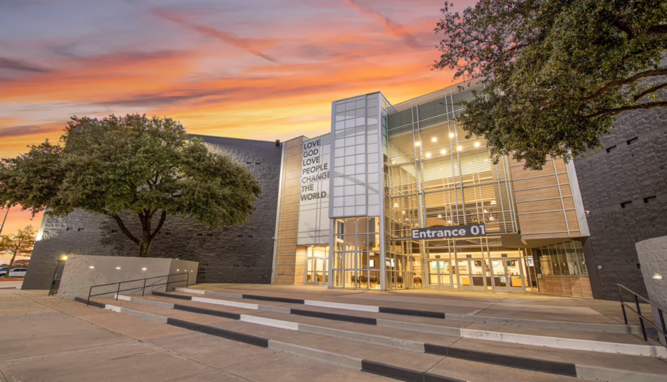 Thousand Hills Church exterior at sunset featuring glass entrance tower and "Love God Love People Change the World" signage — church architects Visioneering Studios