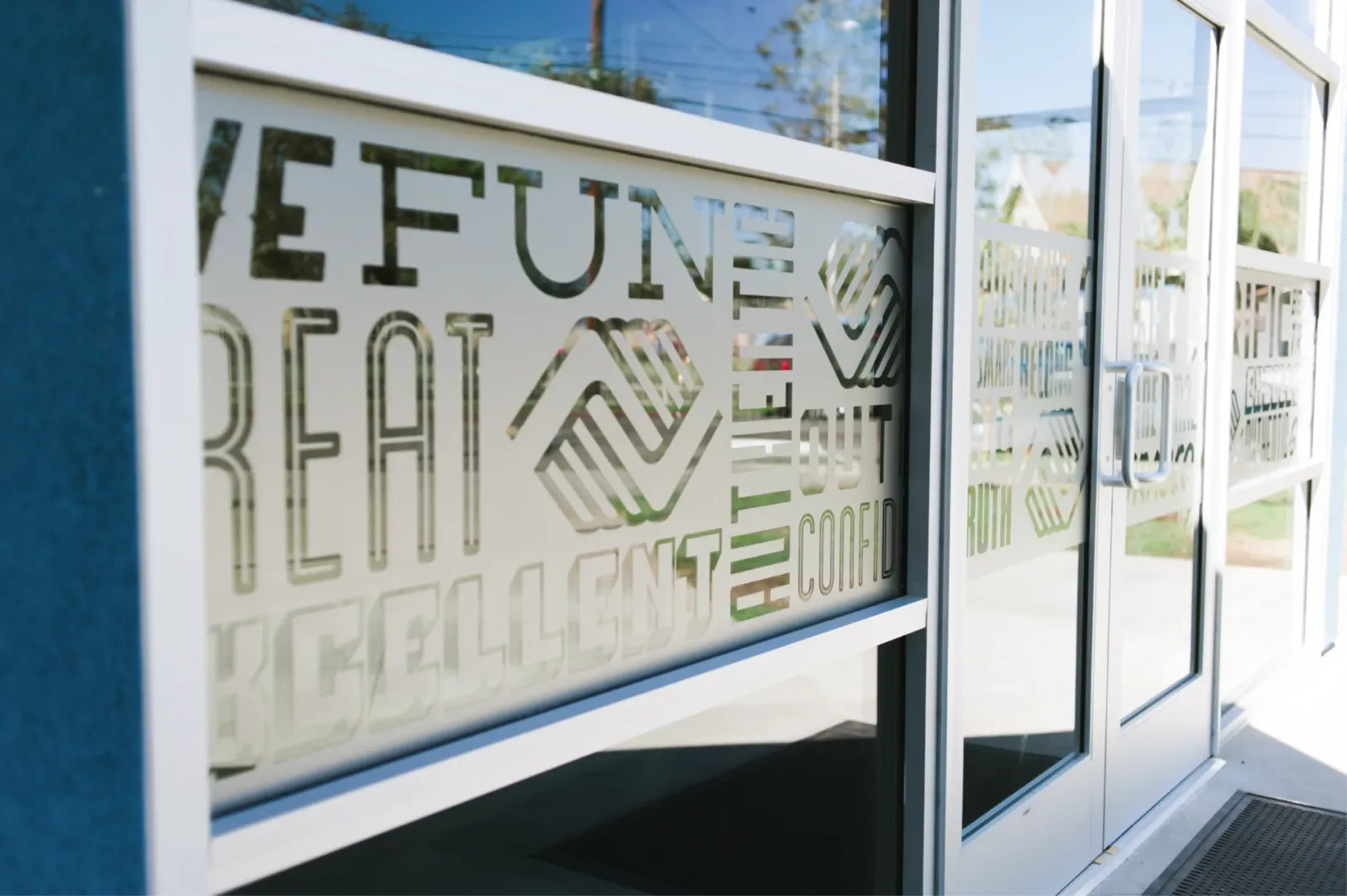 Close-up of exterior door at Boys & Girls Club teen center designed by Visioneering Studios, featuring branded decal with values like 'fun' and 'authentic'.