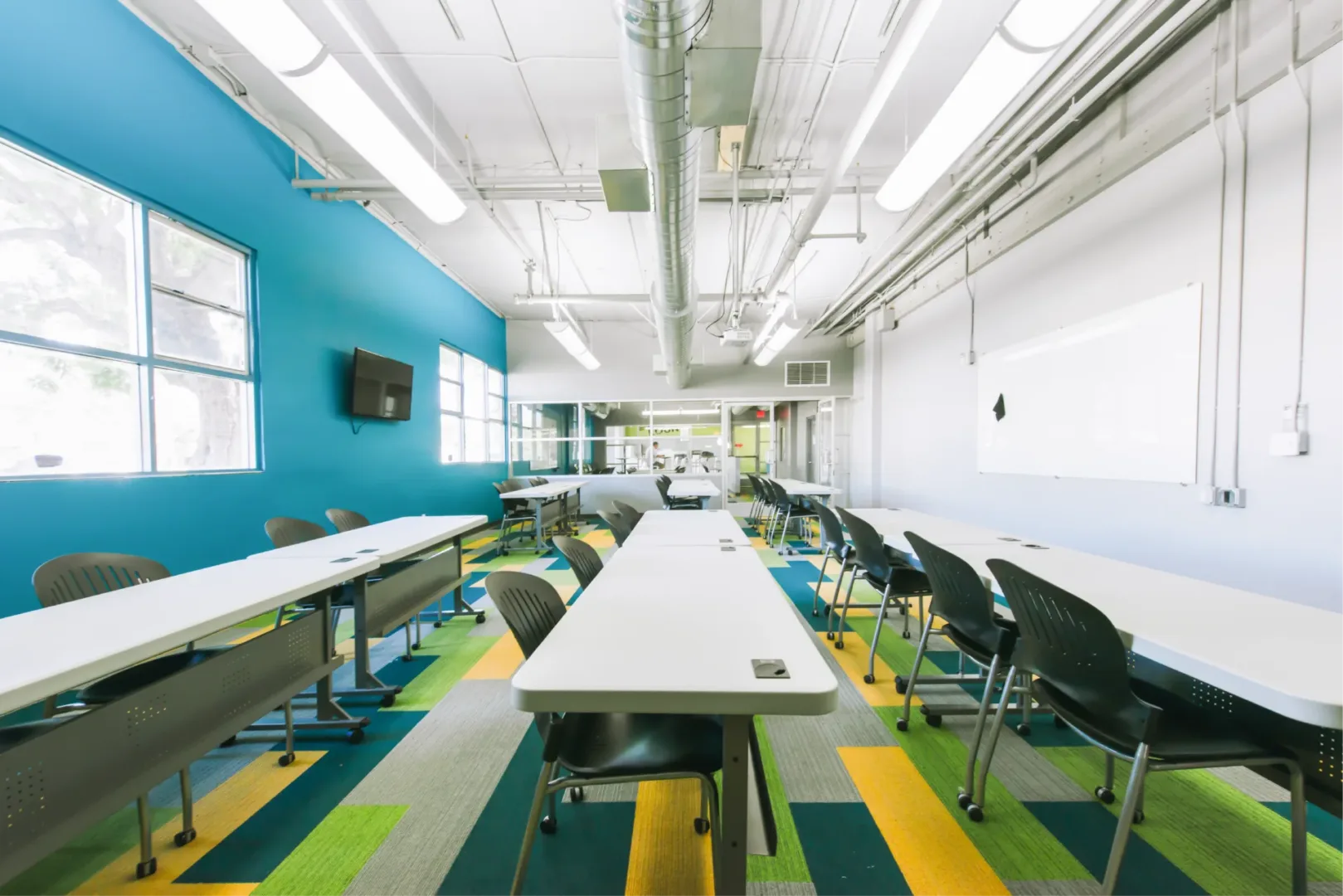 Renovated classroom at Boys & Girls Club teen center interior design by Visioneering Studios, featuring new carpet, fresh paint, whiteboard, and modern furniture.