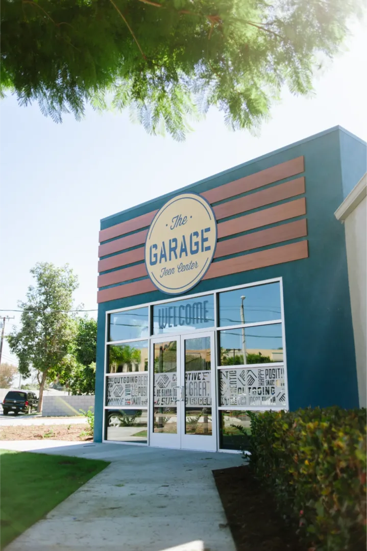 Exterior design of Boys & Girls Club teen center with dark blue facade, 'The Garage' signage, and branded decal entry doors design build firm Visioneering Studios