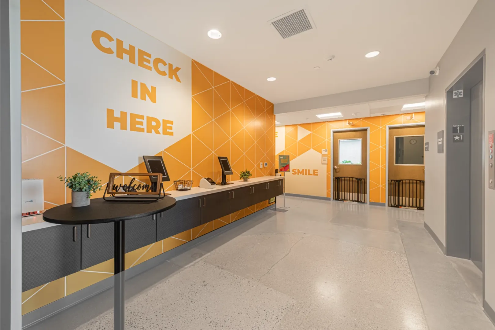 mesa kids check in counter with brand color orange for the kids. this area includes a graphic wall design in the hallways by church build design company visioneering studios