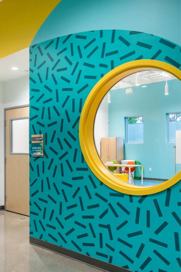 Wall graphic design at Seabreeze Church’s kids building church designer & architect Visioneering Studios, featuring playful circular patterns, a round window offering a peek into a classroom, matching design elements from the kids check-in area, and coordinated room ID signage that flows throughout the space.