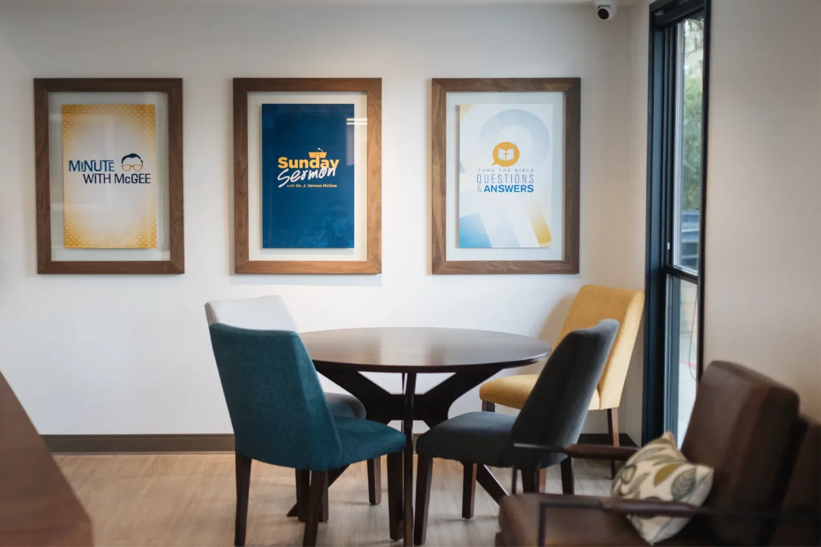 Visioneering Studios (architect firm) designed Thru the Bible’s new headquarters with a welcoming lunch and meeting space featuring a four-seat table, where staff or guests can connect, accented by framed podcast cover art on the wall.