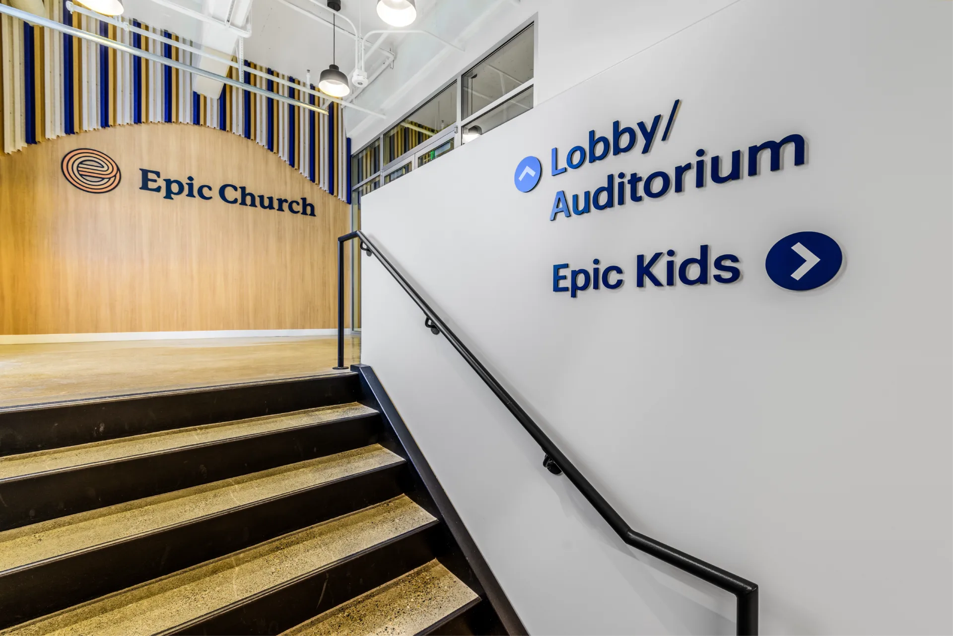 enviropop | visioneering studios partnered helping with wayfinding & graphic solutions. photo featuring epic church logo at top of the stairs which then highlights wayfinding signage at the bottom of the stairs to go to lobby/auditorium or to epic kids at epic church in San Francisco