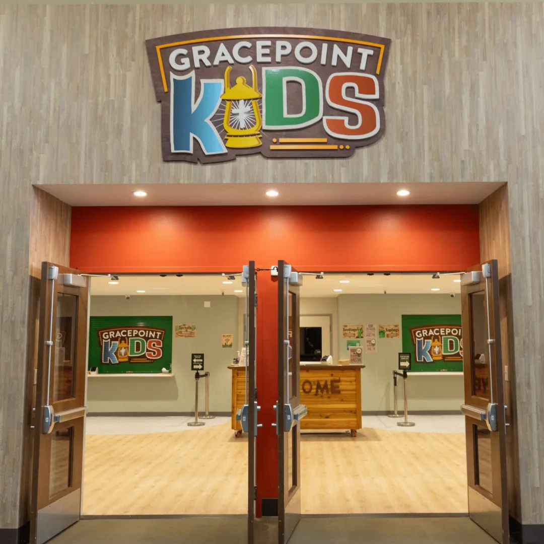 A bold Gracepoint Kids entry featuring double doors, a custom wood-paneled accent wall, and illuminated branded signage welcoming families into the kids ministry space.