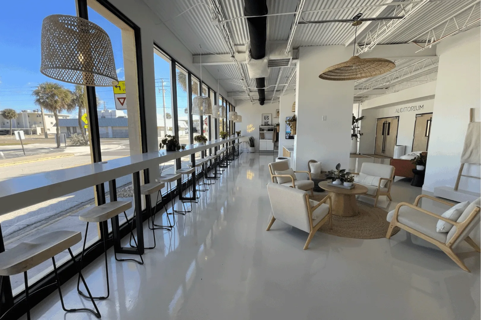 A wide view of the church lobby showcasing high-top seating along floor-to-ceiling windows, coastal-style lounge seating, and natural light filling the space.